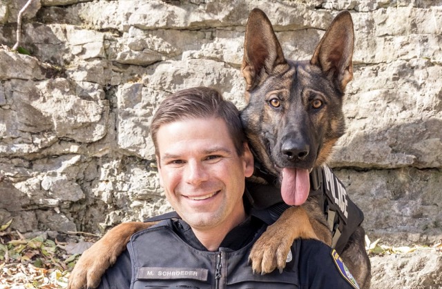 Tango with his handler, Officer Mike Schroeder, in front of a stone wall