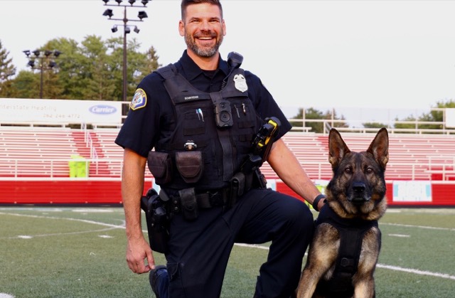 Tango sitting beside an officer on a football field
