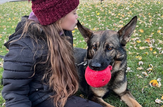 Tango lying in autumn leaves with a red ball while a young fan kisses his head
